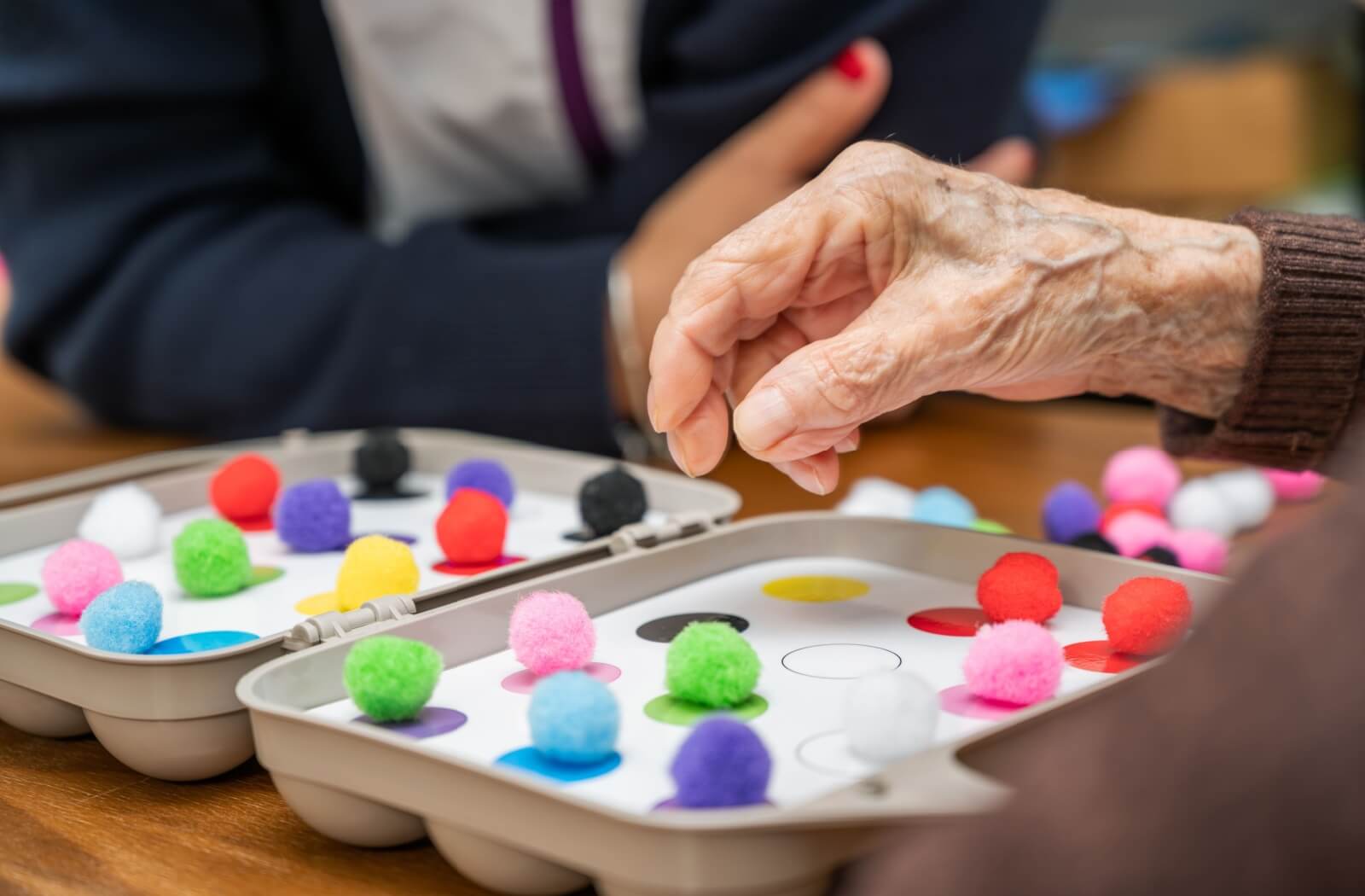 A mature hand matches colorful pompoms to colored spots in cognitive stimulation therapy.