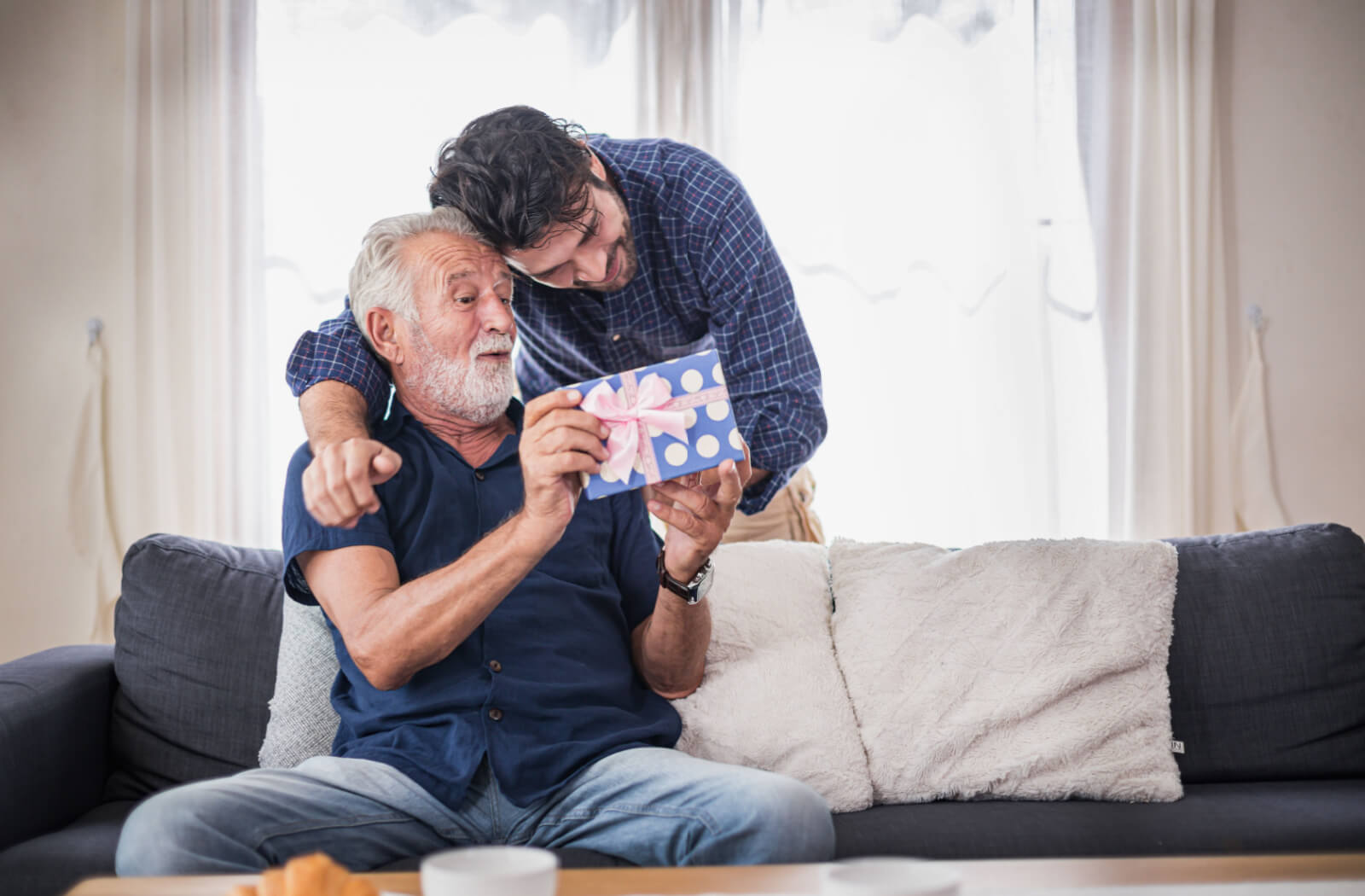 A surprised senior man receiving a gift from his son.