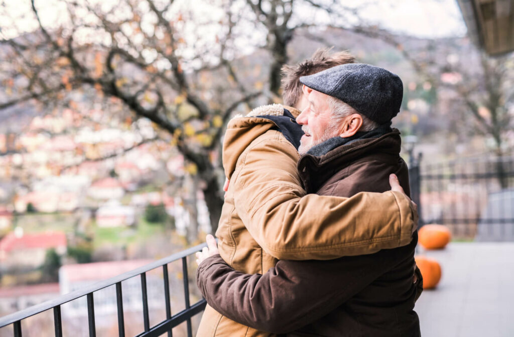 A man hugging his older adult father on a Memory Care  balcony.
